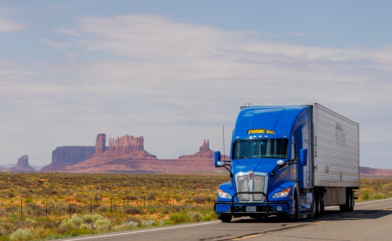 A blue truck travels on the highway with Monument Valleys iconic mesas in the background.