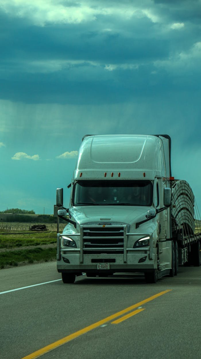 A white semi-truck travels on a highway under a cloudy, dramatic sky.